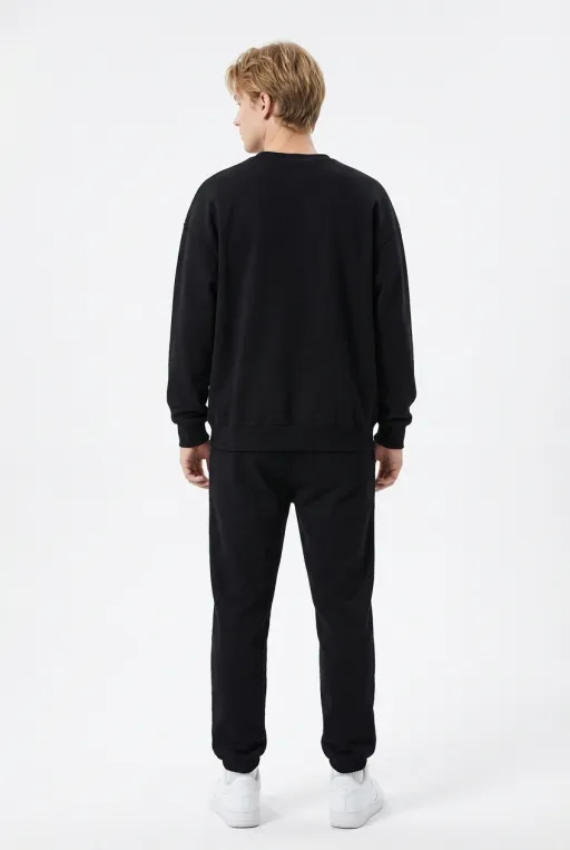 Model wearing black oversized crewneck sweatshirt and jogger set, back view with white sneakers