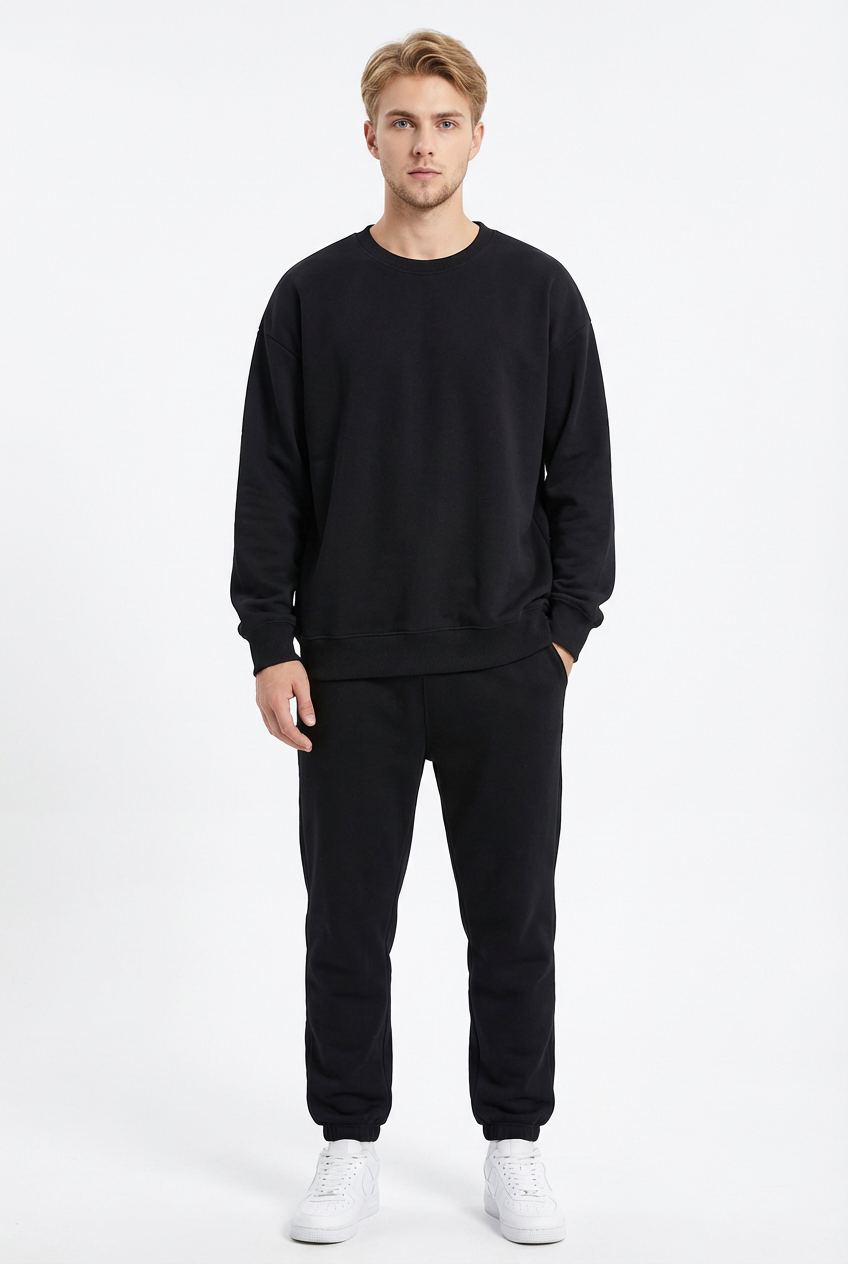 Model wearing black oversized crewneck sweatshirt and jogger set, front view with one hand in pocket