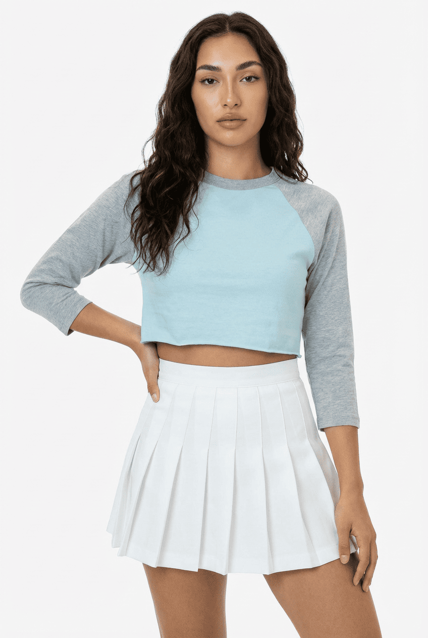 Model wearing light blue and grey raglan 3/4 sleeve cropped top, front view with white pleated mini skirt