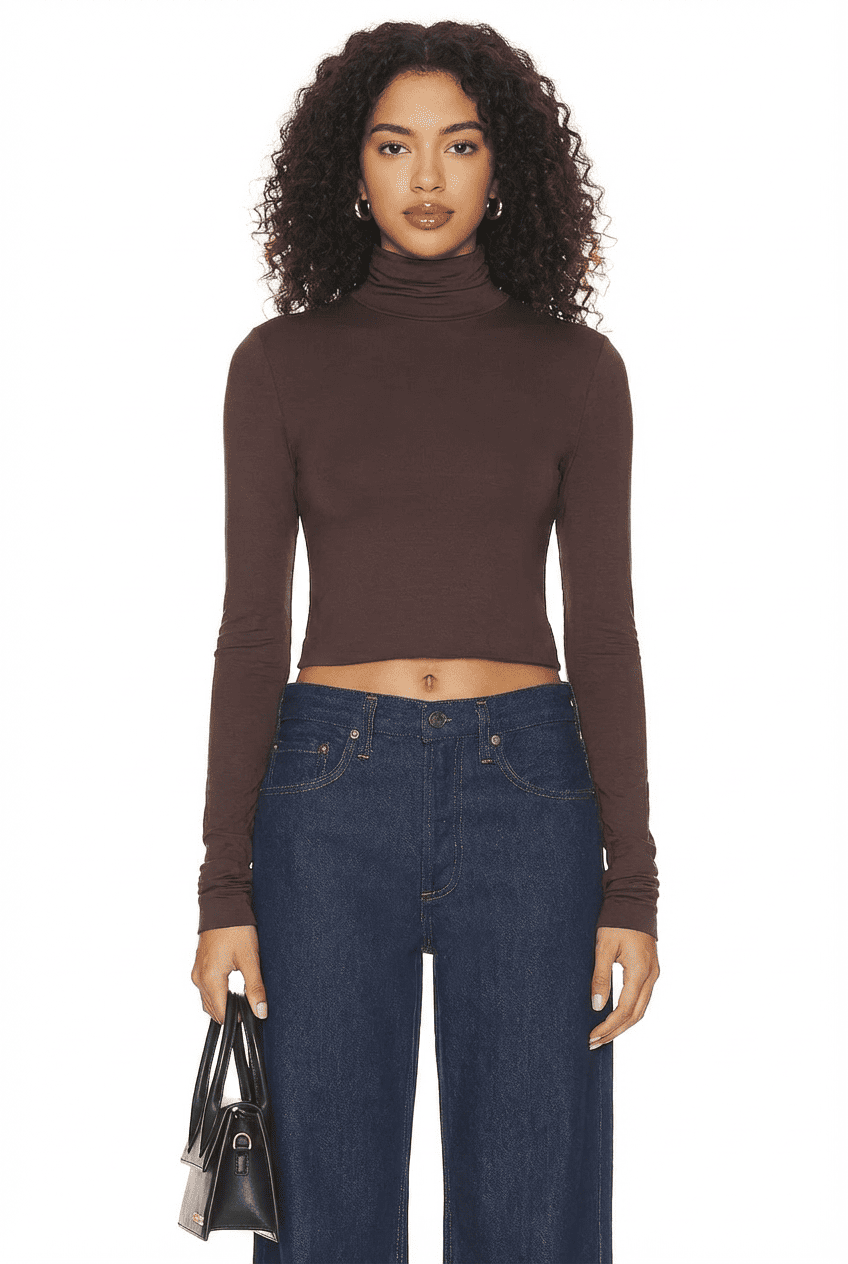 Model wearing chocolate brown slim-fit cropped turtleneck top, front view with dark wide-leg jeans and black handbag