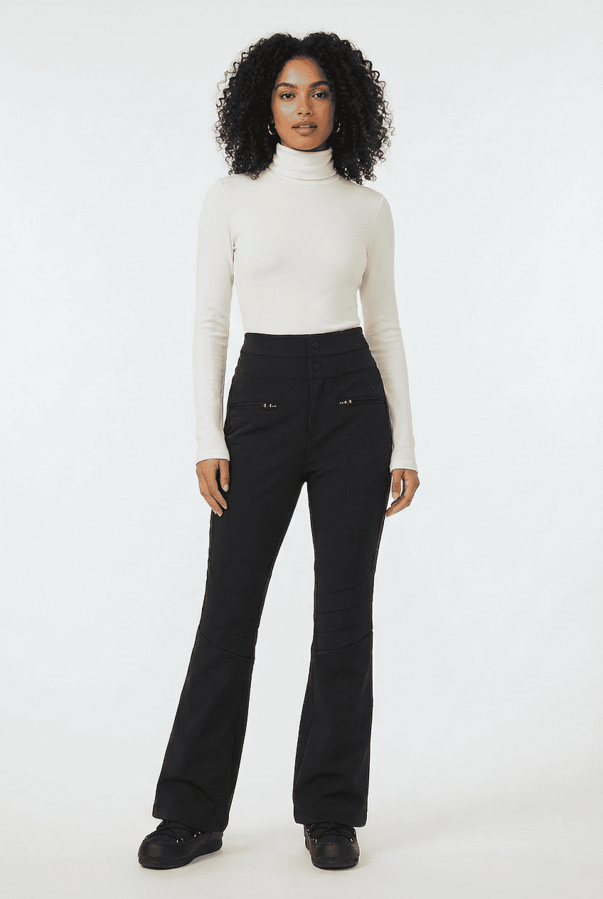 Model wearing black high-waisted flared ski pants, front view styled with a white ribbed turtleneck top and black ski boots