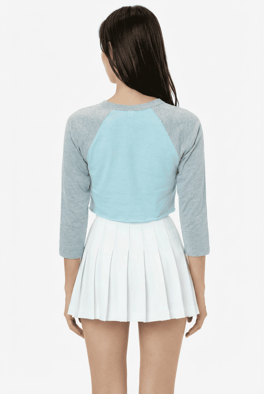Model wearing light blue and grey raglan 3/4 sleeve cropped top, back view with white pleated mini skirt