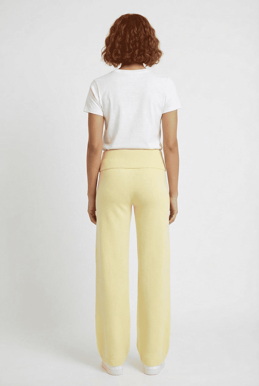 Model wearing butter yellow knit wide-leg trousers, back view styled with a white crewneck tee and white sneakers