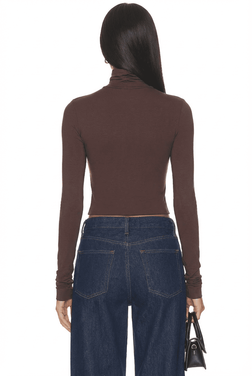 Model wearing chocolate brown slim-fit cropped turtleneck top, back view with dark wide-leg jeans and black handbag