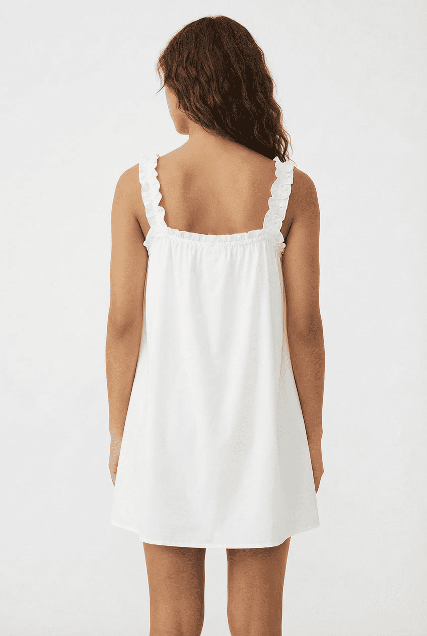 Model wearing white cotton mini slip dress, back view featuring ruffled spaghetti straps and an open-back design
