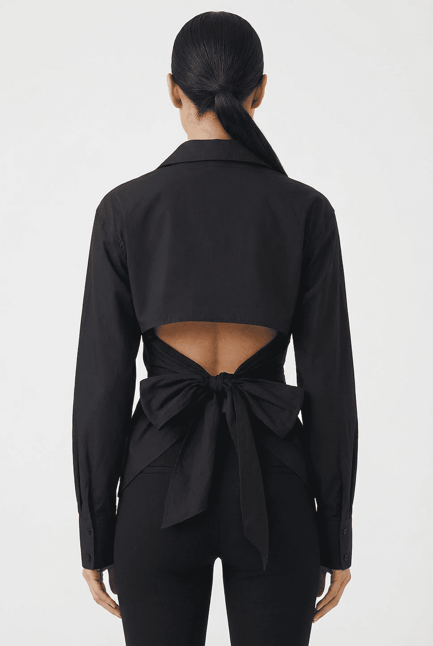 Model wearing black collared shirt with open-back and oversized bow-tie detail, back view paired with black high-waisted leggings